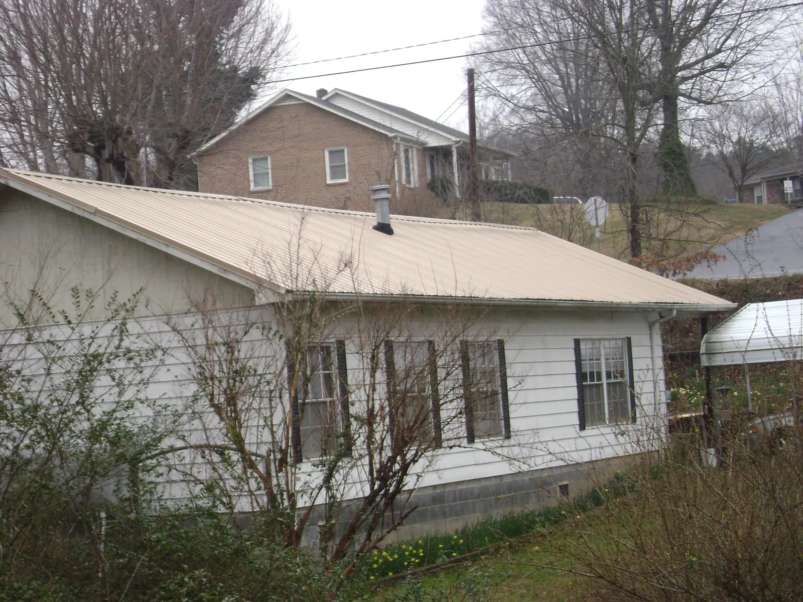 Tan metal roof on a white sided house set into a hillside — Commercial Roofing by Roofing Brothers in Ashwood
